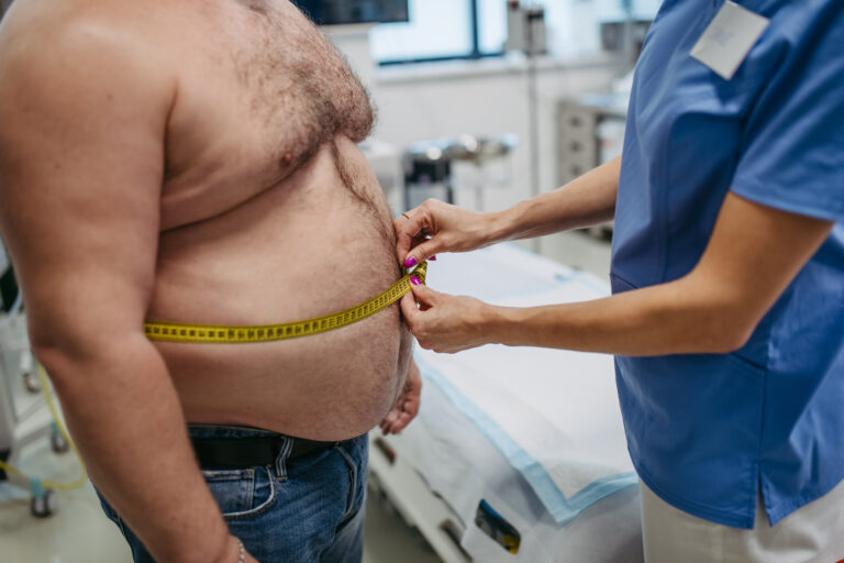 Female doctor measuring waist of overweight patient using tape measure. Obesity affecting middle-aged men's health. Concept of health risks of overwight and obesity